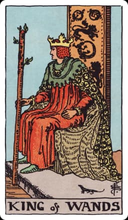 The King of Wands from the Rider-Waite-Smith deck: a king sits sideways on a throne carved with lions and salamanders, wearing a robe patterned with salamanders, holding a budding wand upright, a small salamander visible near the base of his throne, a desert landscape stretching behind him.