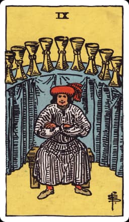 The Nine of Cups from the Rider-Waite-Smith deck: a well-dressed, self-satisfied man sits with arms crossed on a wooden bench, smiling, before a curved shelf draped in blue cloth displaying nine golden cups arranged in a wide arc behind him.