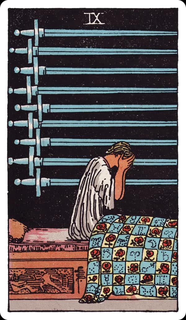 The Nine of Swords from the Rider-Waite-Smith deck: a figure sits upright in bed at night, head buried in both hands, nine swords mounted horizontally on the dark wall behind them, the quilt below decorated with roses and astrological symbols, a carved panel on the bed showing one figure attacking another.