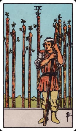 The Nine of Wands from the Rider-Waite-Smith deck: a bandaged man leans warily on a single upright wand, glancing back over his shoulder, while eight other wands stand planted behind him in a fence-like row, his stance guarded and his posture tired but unbroken.