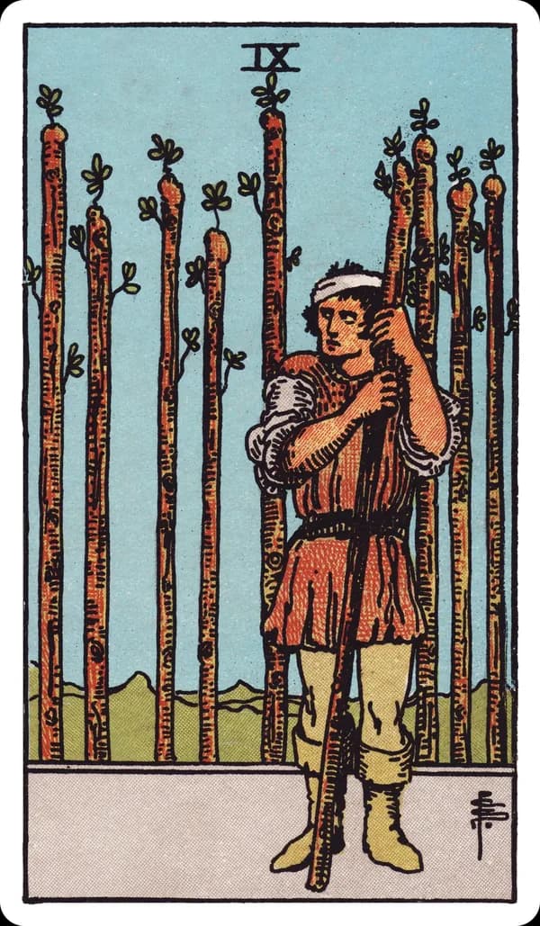 The Nine of Wands from the Rider-Waite-Smith deck: a bandaged man leans warily on a single upright wand, glancing back over his shoulder, while eight other wands stand planted behind him in a fence-like row, his stance guarded and his posture tired but unbroken.