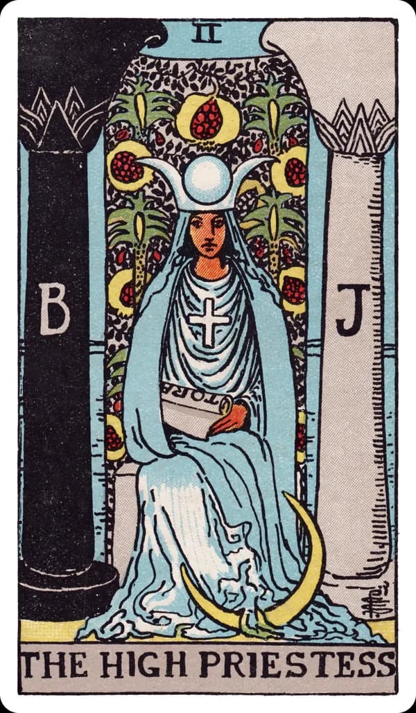 The High Priestess from the Rider-Waite-Smith deck: a robed woman sits enthroned between two pillars marked B and J (Boaz and Jachin), a veil embroidered with pomegranates hanging behind her, a crescent moon resting at her feet, a horned lunar headdress with a solar disc crowning her head, a solar cross on her chest, and a partially-hidden scroll marked TORA resting in her lap.